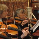 Three women play violin together