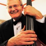 An older man smiling while holding his upright bass