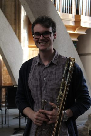 Joe Hillyard holds a trombone and smiles at the camera
