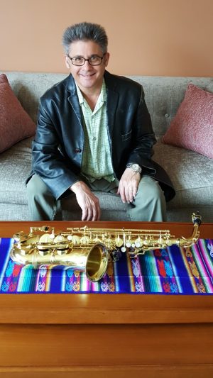 David Trooper sits on a couch with his saxophone on a table in front of him